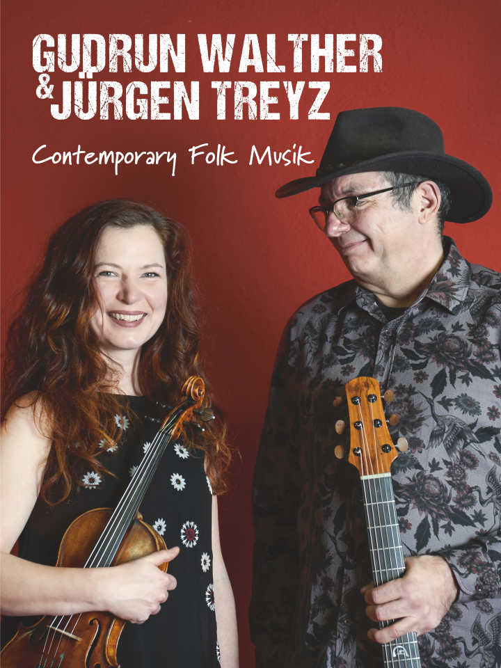 Links lächelt Gudrun Walther mit rot wallendem Haar, ihre Geige in der Hand. Rechts steht Juuml;rgen Treyz mit Gitarre in der Hand und Hut auf dem Kopf. Er lächelt zu ihr hin.